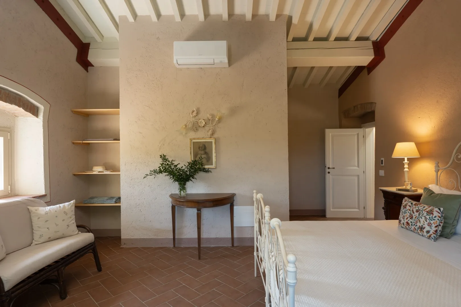Un dormitorio con una cama, una lámpara de noche y una mesita junto a una pared central.