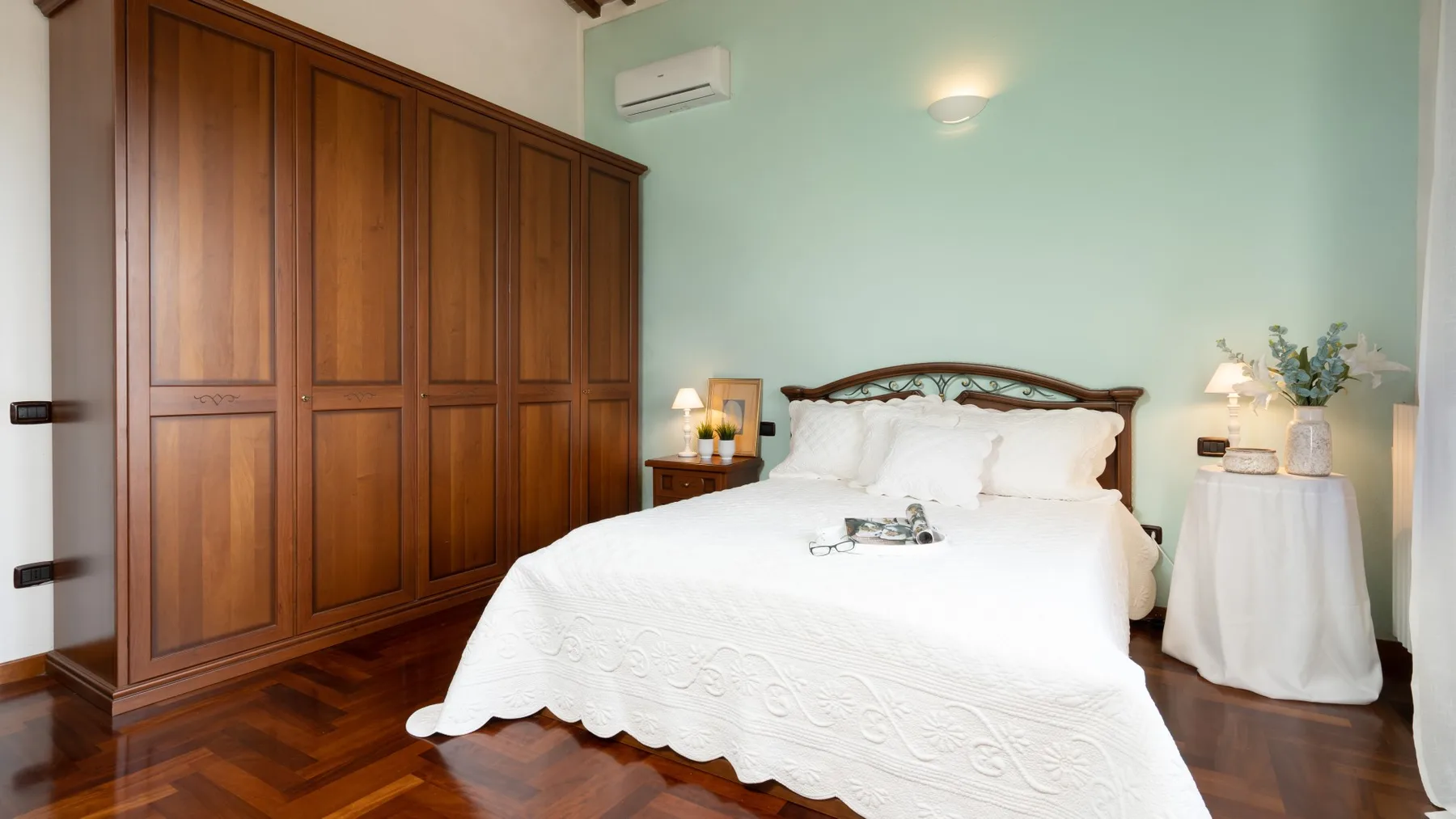 Un dormitorio con una cama blanca, un armario de madera y mesillas de noche.