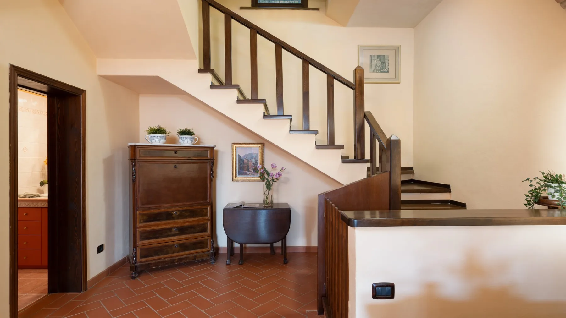 Una escalera interior sube sobre una entrada embaldosada con un mueble de madera.