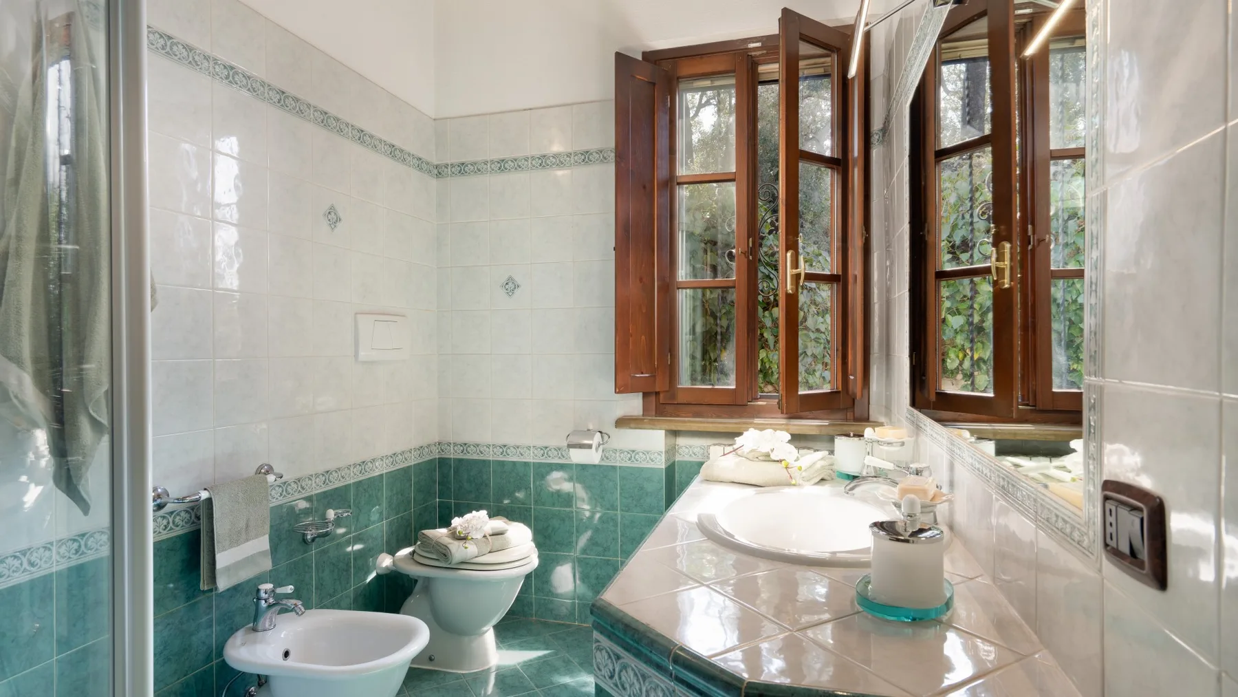 Un baño de azulejos con lavabo, inodoro y ventanas de madera.