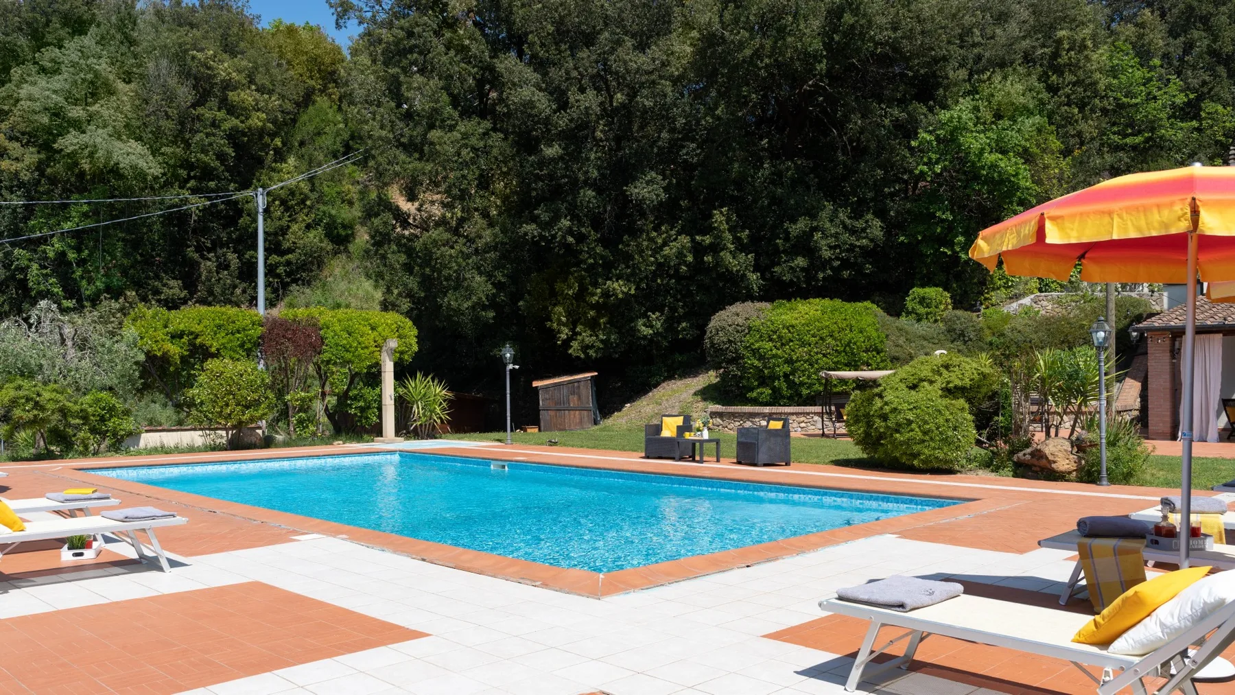 Una piscina al aire libre está rodeada de una terraza pavimentada y asientos.
