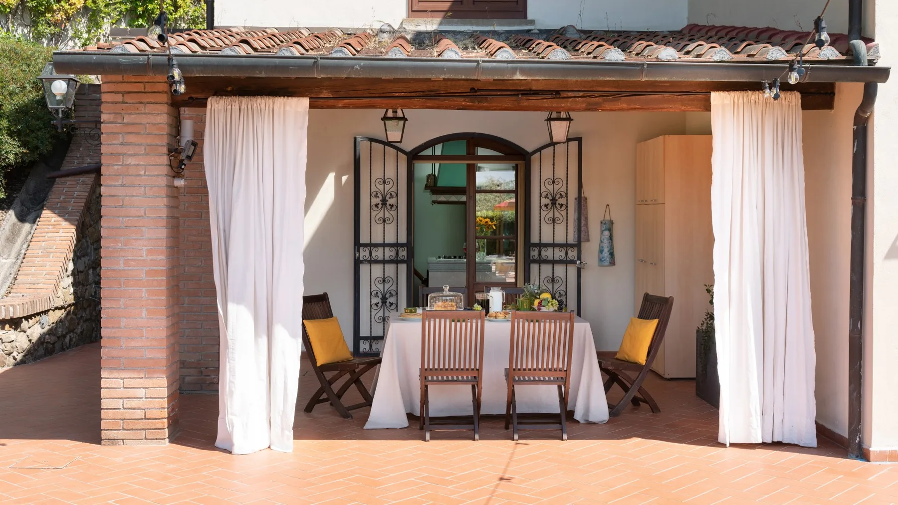 Comedor exterior cubierto con una mesa y sillas junto a cortinas abiertas.