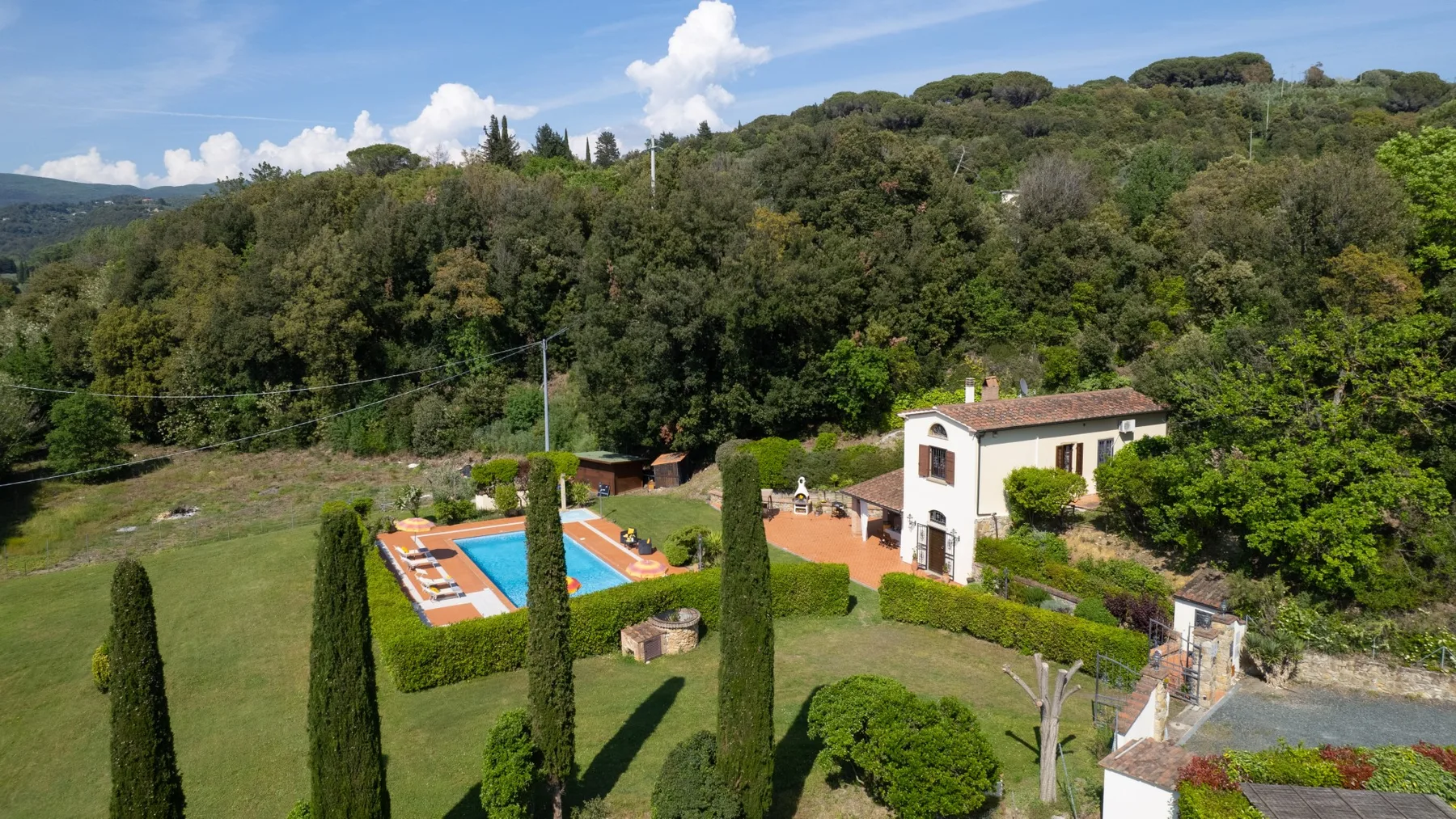 Una villa rural junto a una piscina está rodeada de jardines y colinas boscosas.