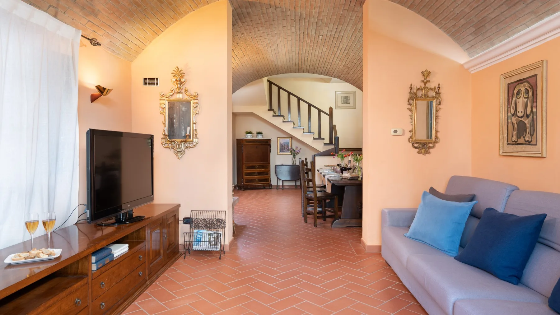 Una sala de estar con televisión, asientos y una escalera al fondo.