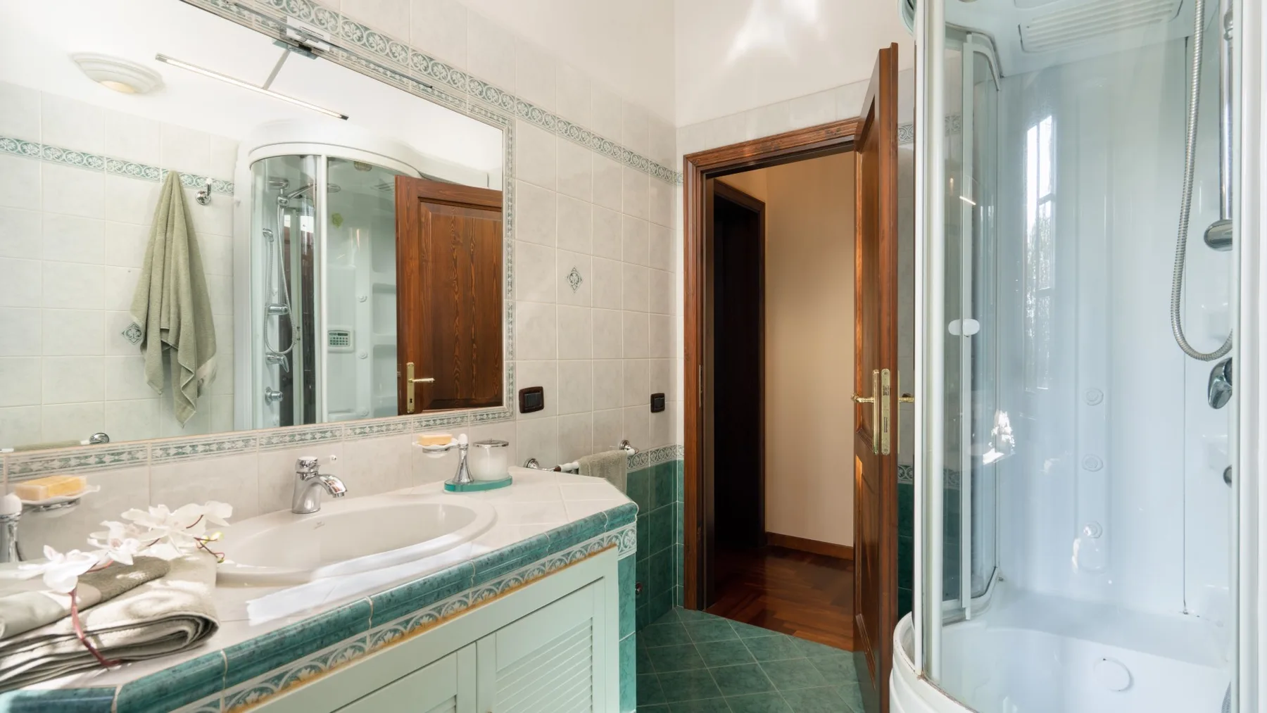 Un baño alicatado con lavabo, espejo amplio y ducha de cristal.