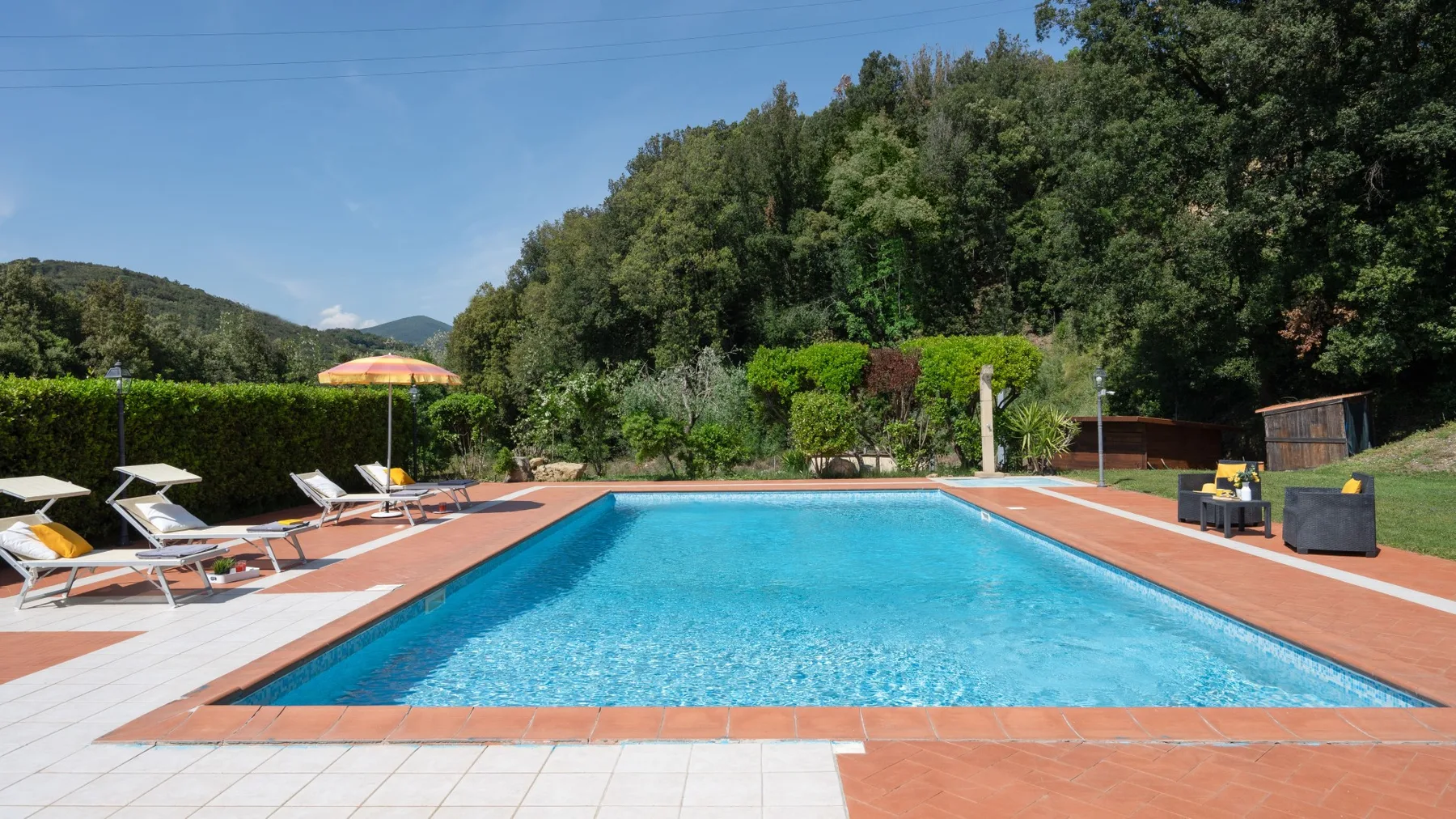 Una piscina al aire libre ocupa una terraza pavimentada junto a colinas boscosas.