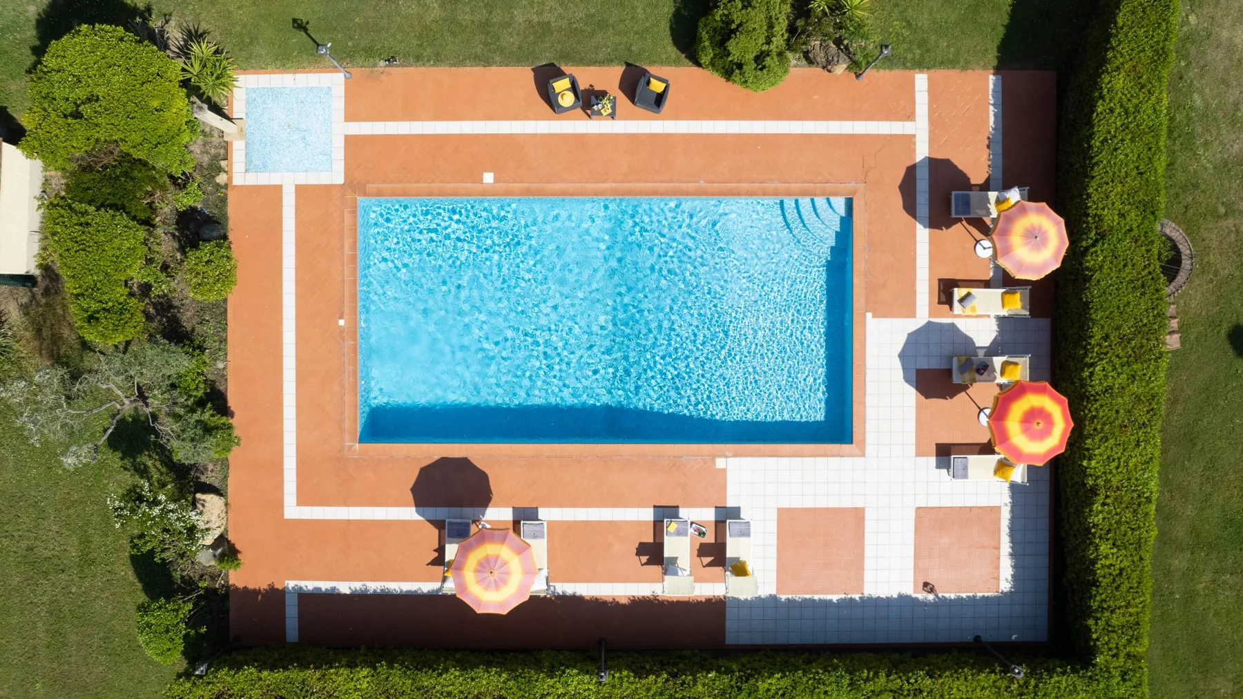 Vista aérea de una piscina al aire libre rodeada por una terraza pavimentada.