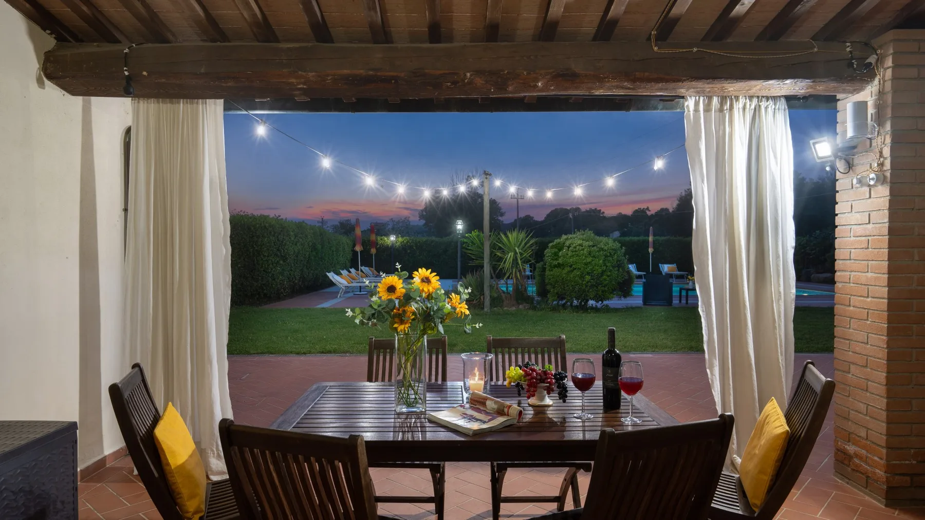 Un comedor exterior cubierto se abre a un jardín al anochecer.