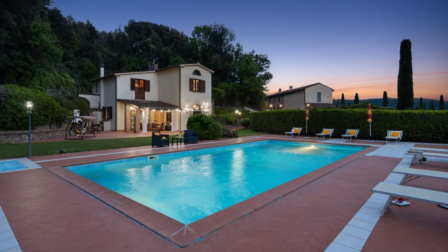 Una piscina al aire libre junto a una casa, con árboles y colinas al fondo.