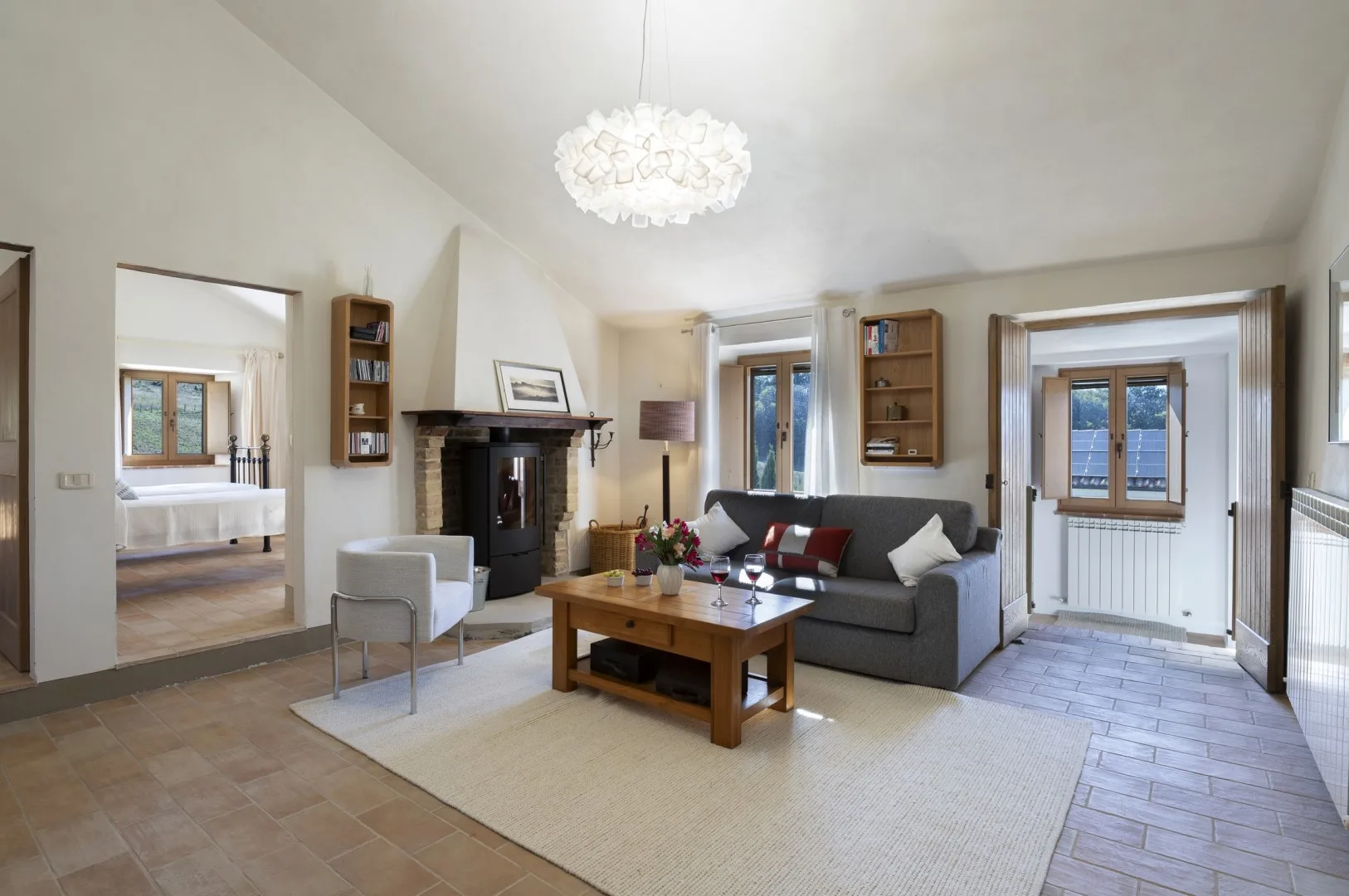 Una sala luminosa cuenta con un sofá gris, una chimenea oscura y una mesa de centro de madera sobre una alfombra amplia.