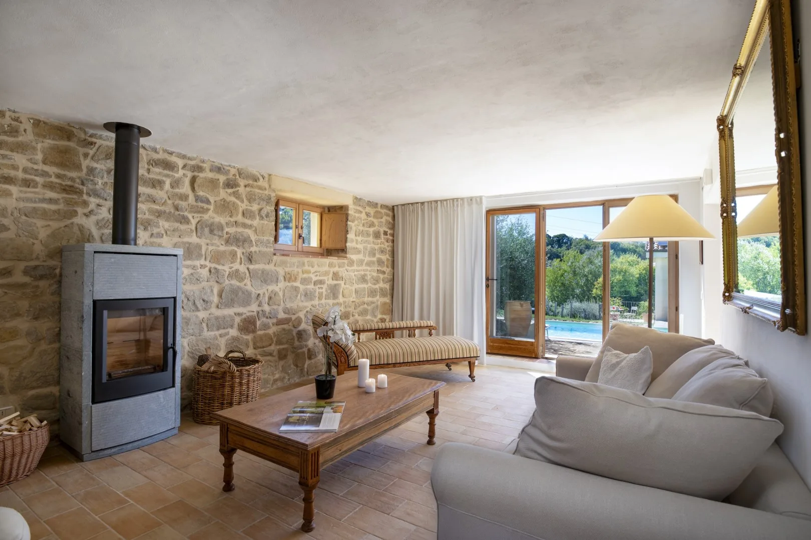 Sala de estar con pared de piedra, estufa de leña, sofá, mesa de centro y puertas acristaladas que dan a un patio.