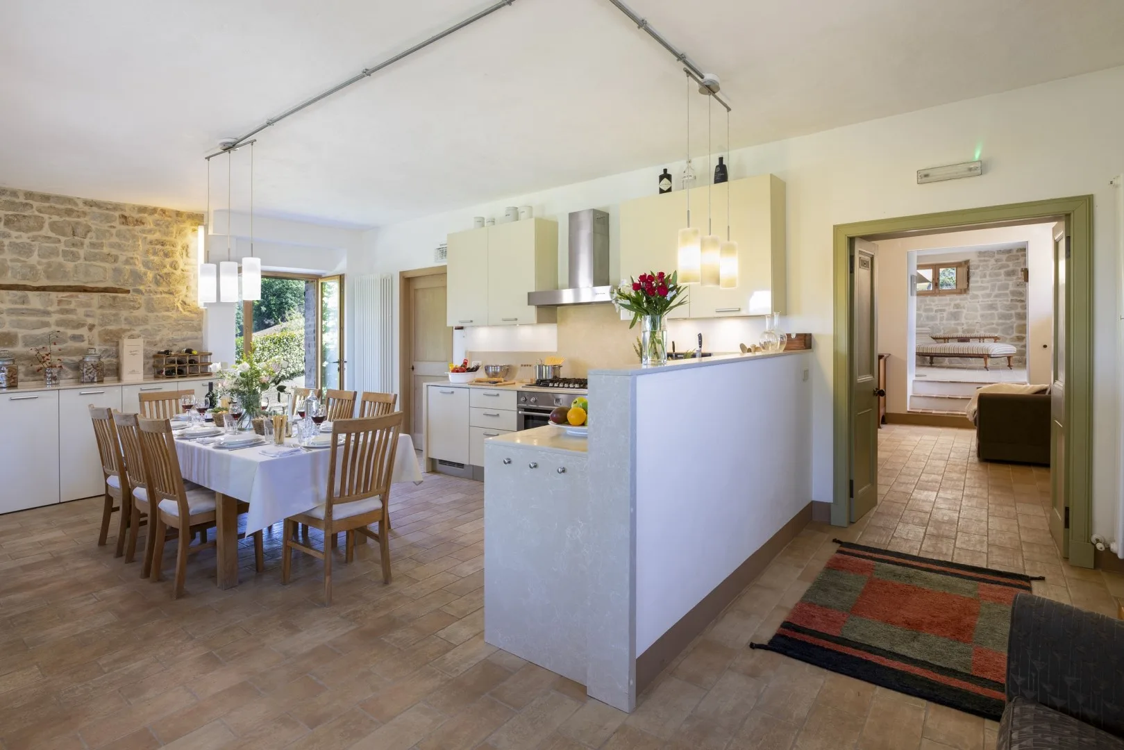 Una luminosa cocina-comedor de planta abierta cuenta con una isla blanca, una mesa puesta y una pared de piedra vista.