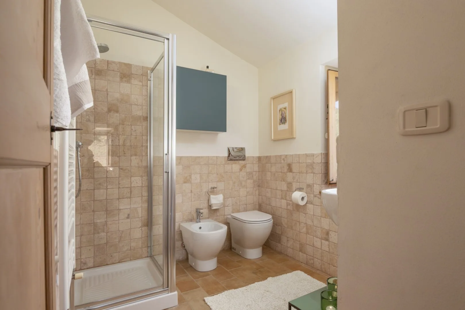 Un baño alicatado tiene una ducha con mampara de vidrio, inodoro, bidé y armario de pared.