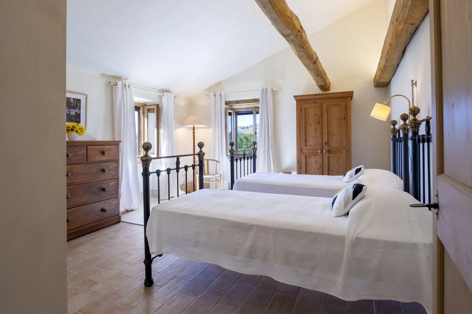 Un dormitorio luminoso con dos camas, vigas de madera vistas y un armario alto de madera.