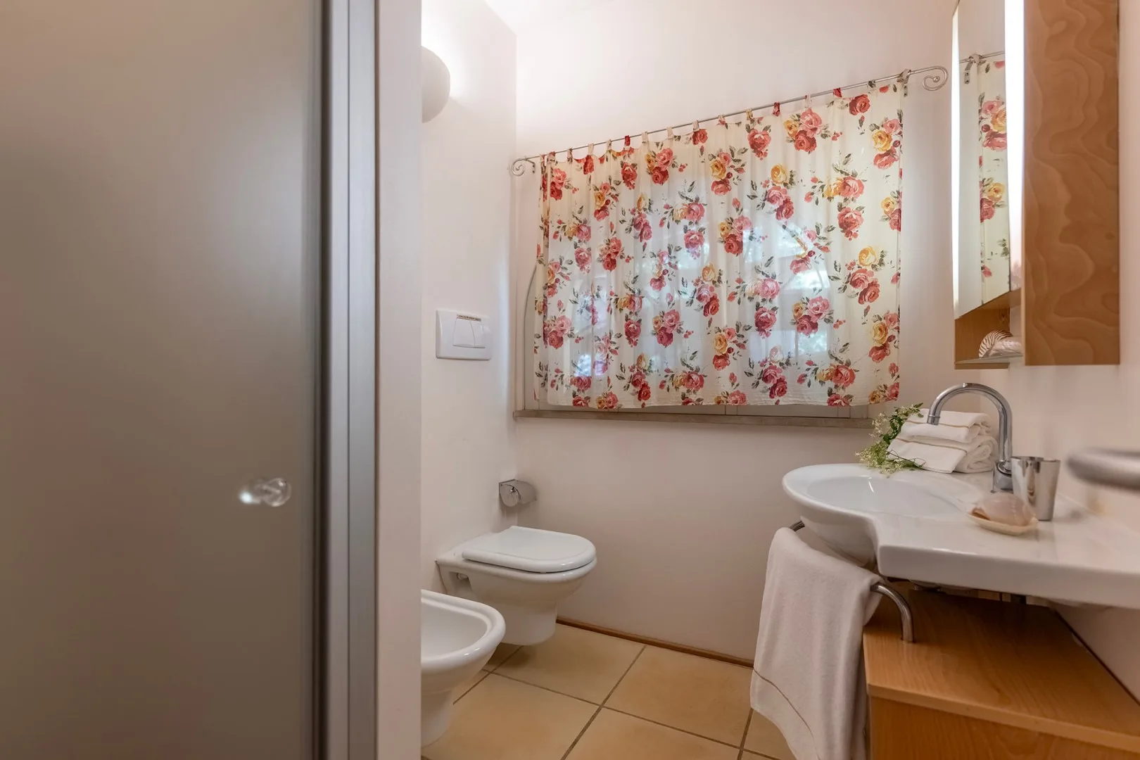 Un baño con cortina floral, lavabo e inodoro.
