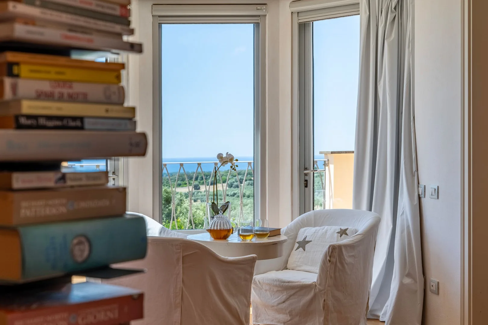 Una luminosa zona de estar con asientos acolchados junto a ventanas altas con vistas a vegetación y al mar.