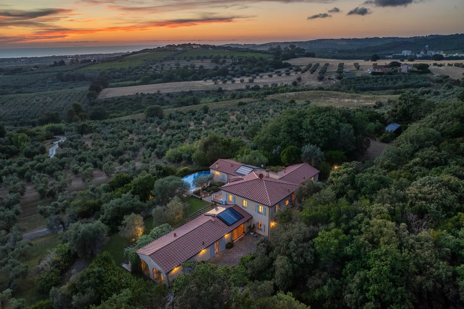 Vista aérea de una casa rural entre campos y árboles al atardecer.