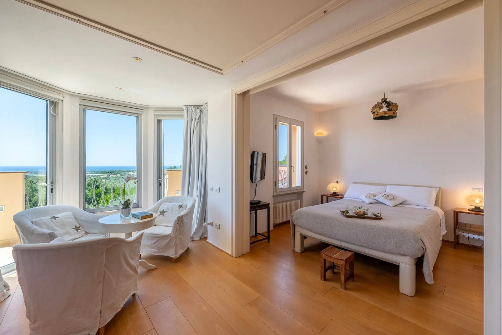 Un dormitorio luminoso con una cama y una pequeña zona de estar junto a grandes ventanas.