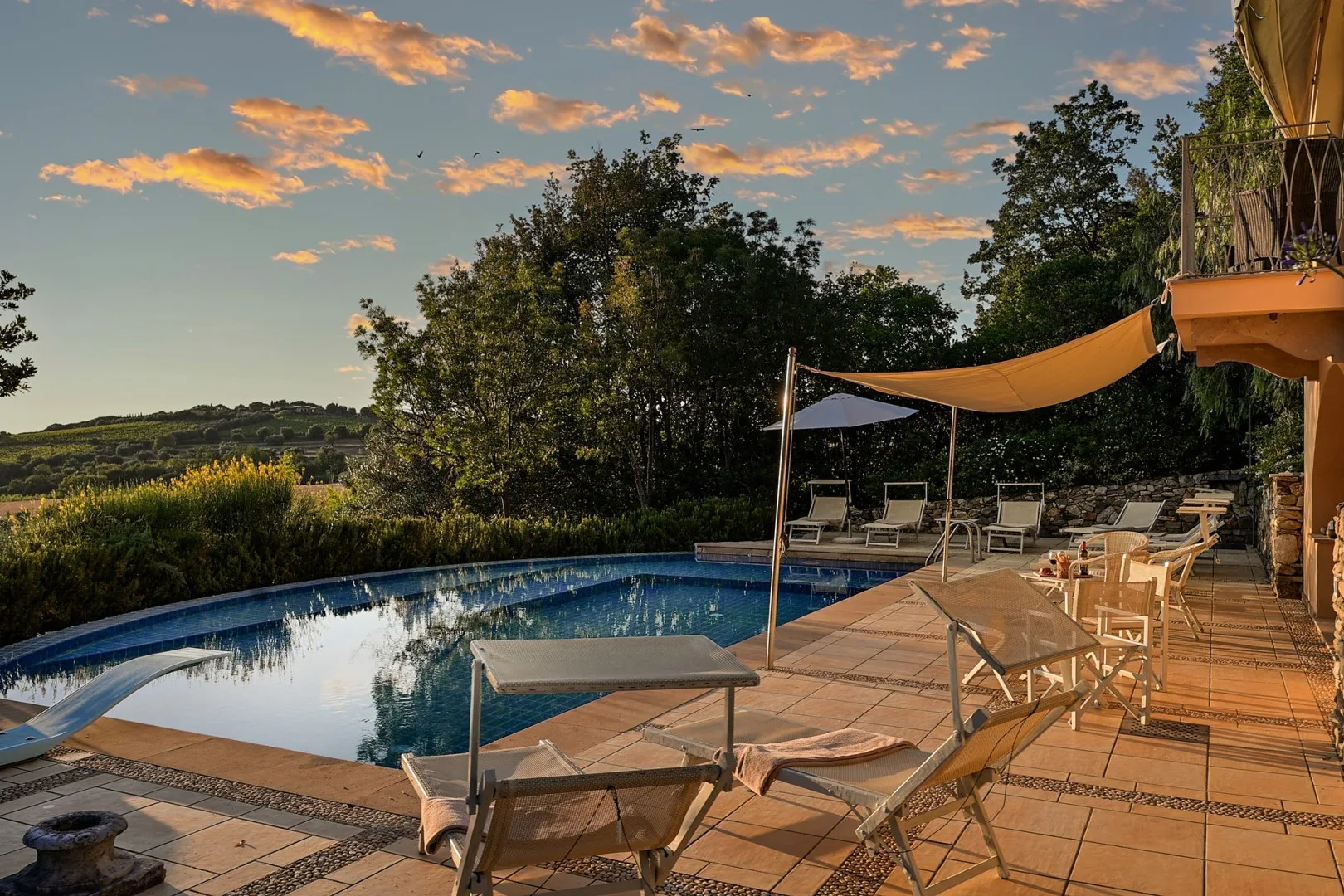 Una piscina al aire libre junto a un patio embaldosado con asientos y una cubierta de sombra.