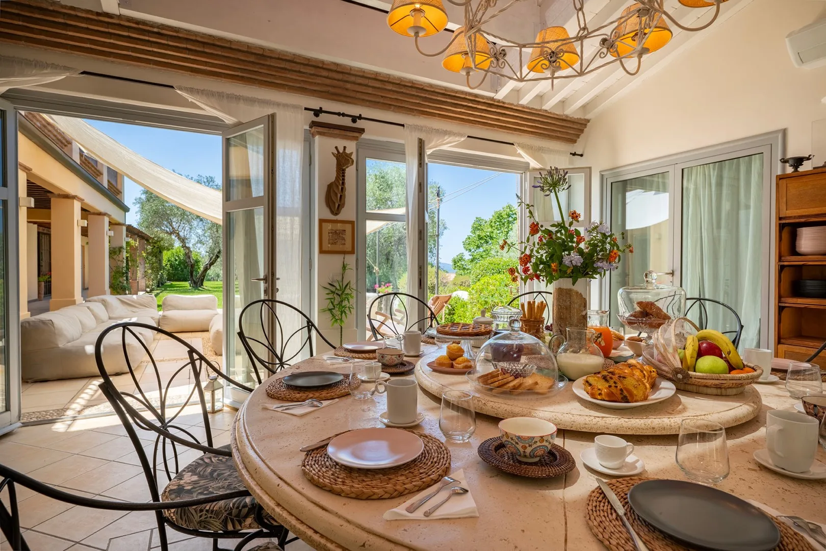 Comedor con una mesa puesta junto a puertas abiertas que dan a un jardín.