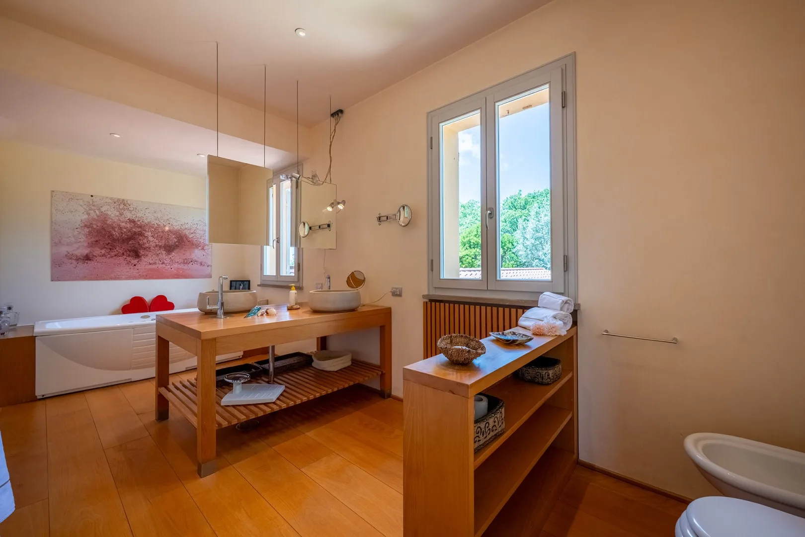 Un baño con bañera, estanterías de madera y dos ventanas.