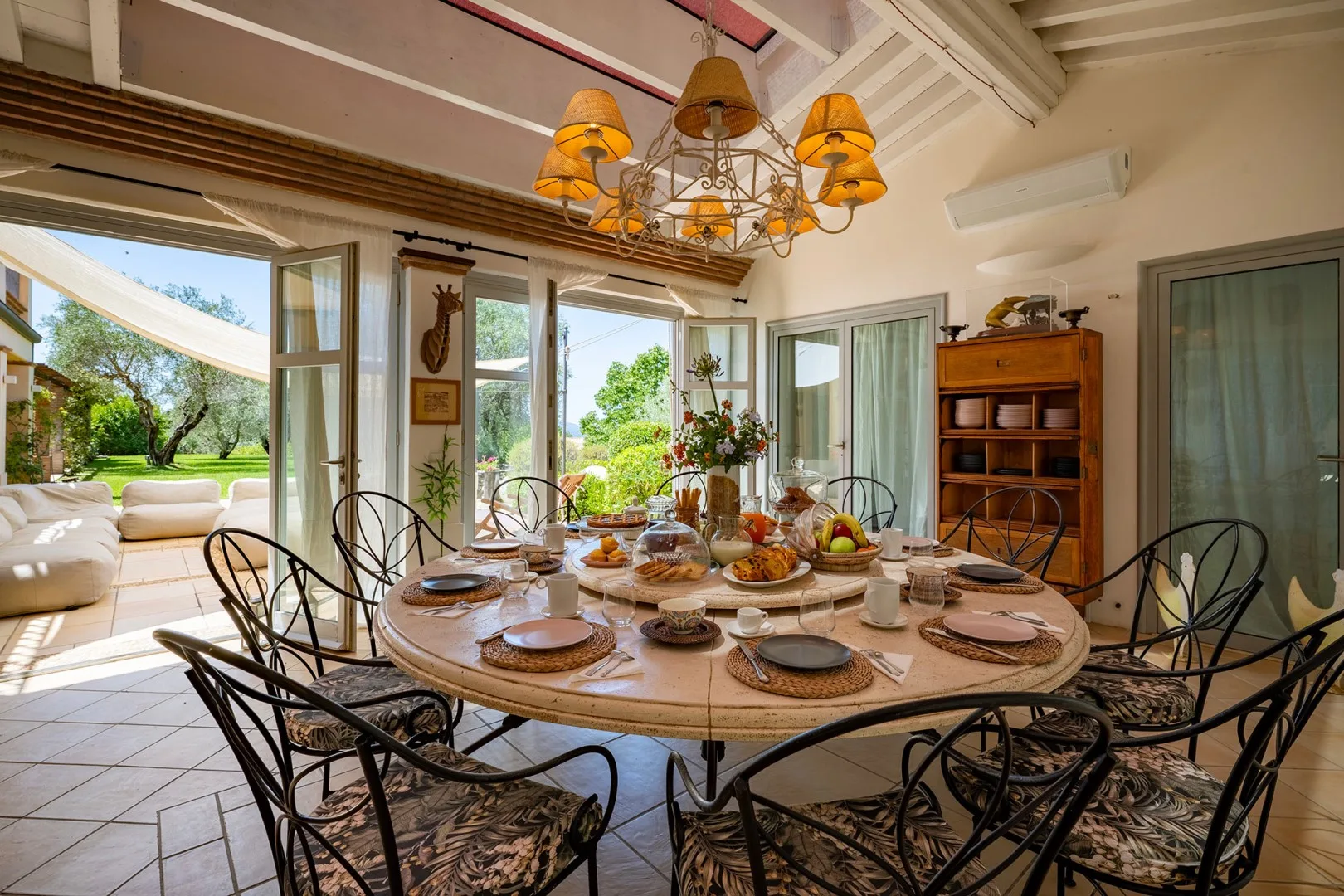Comedor con una mesa grande preparada, asientos oscuros y vistas abiertas al jardín.