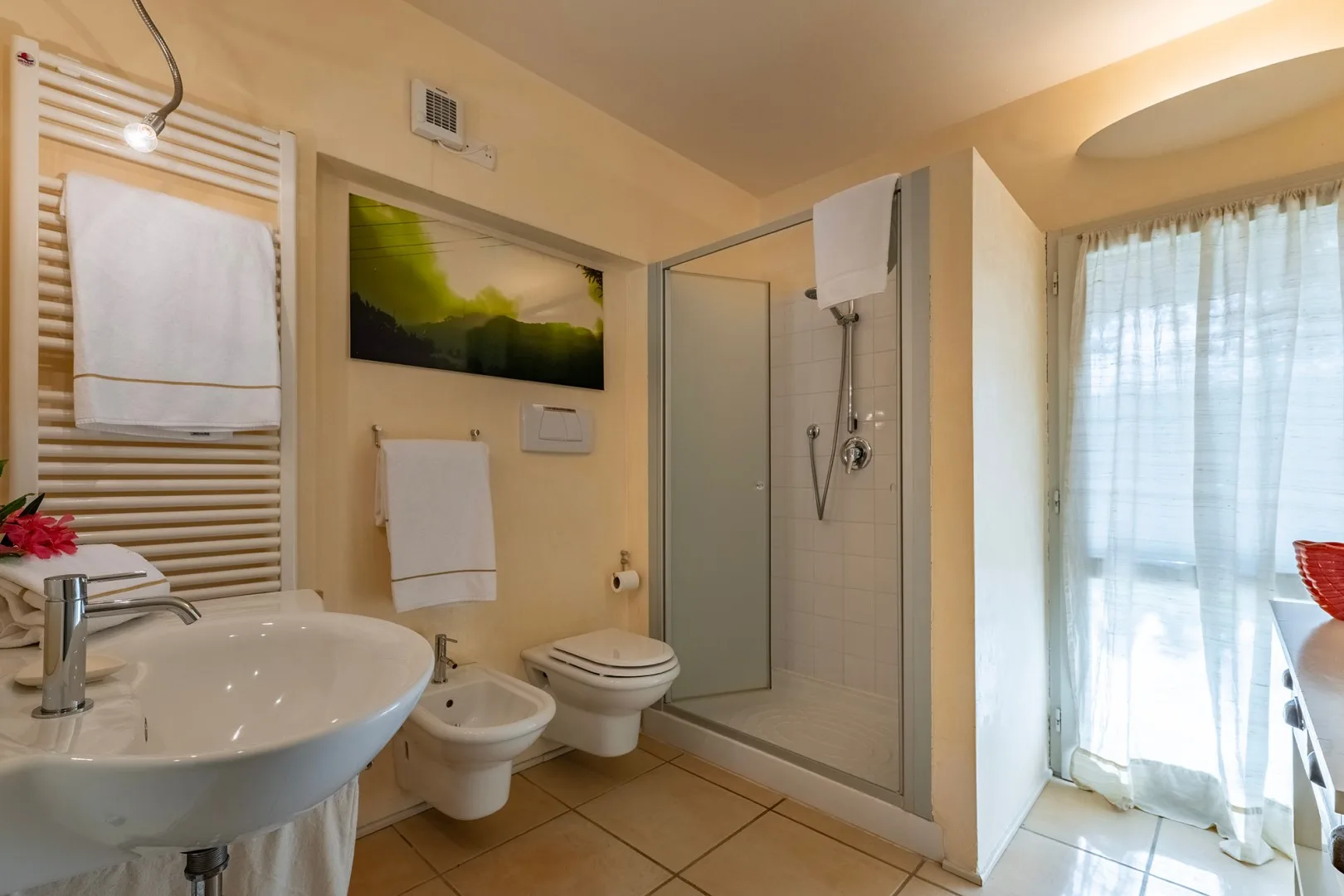 Un baño con lavabo, inodoro y ducha de vidrio junto a una ventana con cortinas.