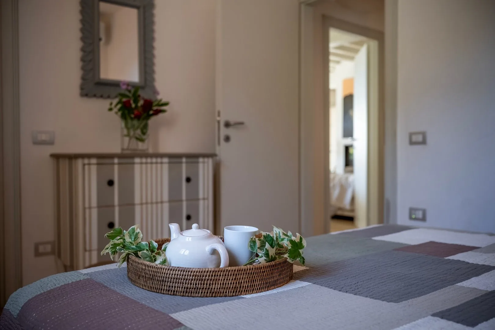 Un dormitorio con una cama en primer plano y una cómoda decorada con flores.