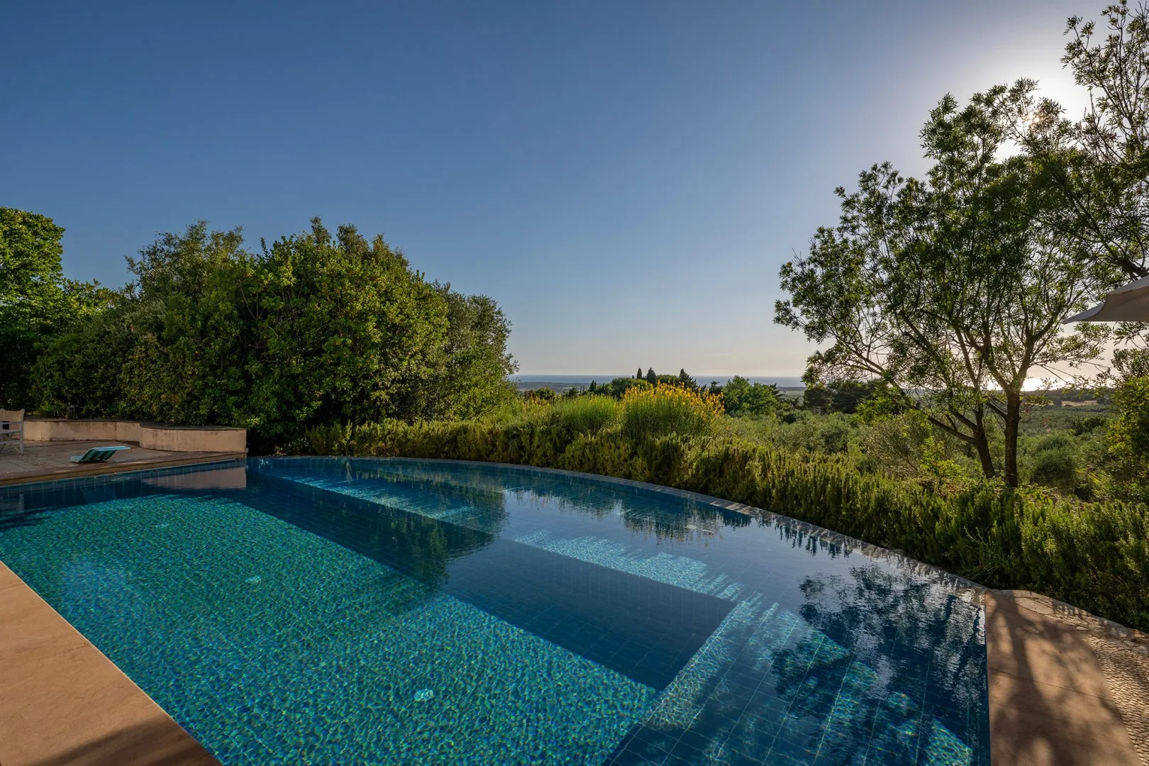 Una piscina al aire libre está rodeada de vegetación, con el mar visible al fondo.