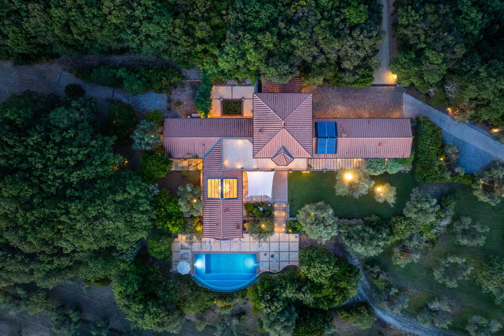 Vista aérea de una casa rodeada de árboles, con una piscina.