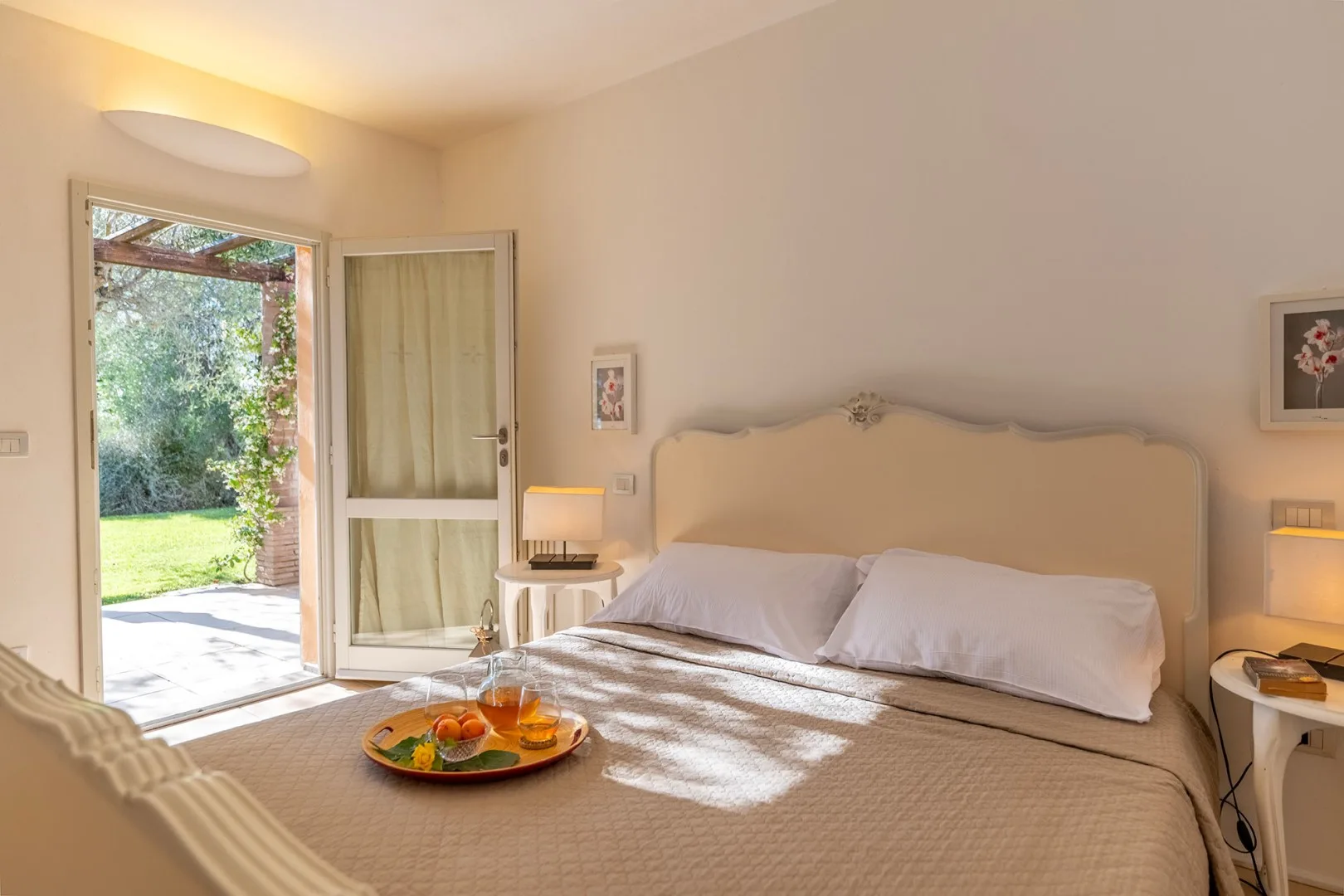 Un dormitorio luminoso con una cama junto a una puerta de vidrio abierta y vegetación al fondo.