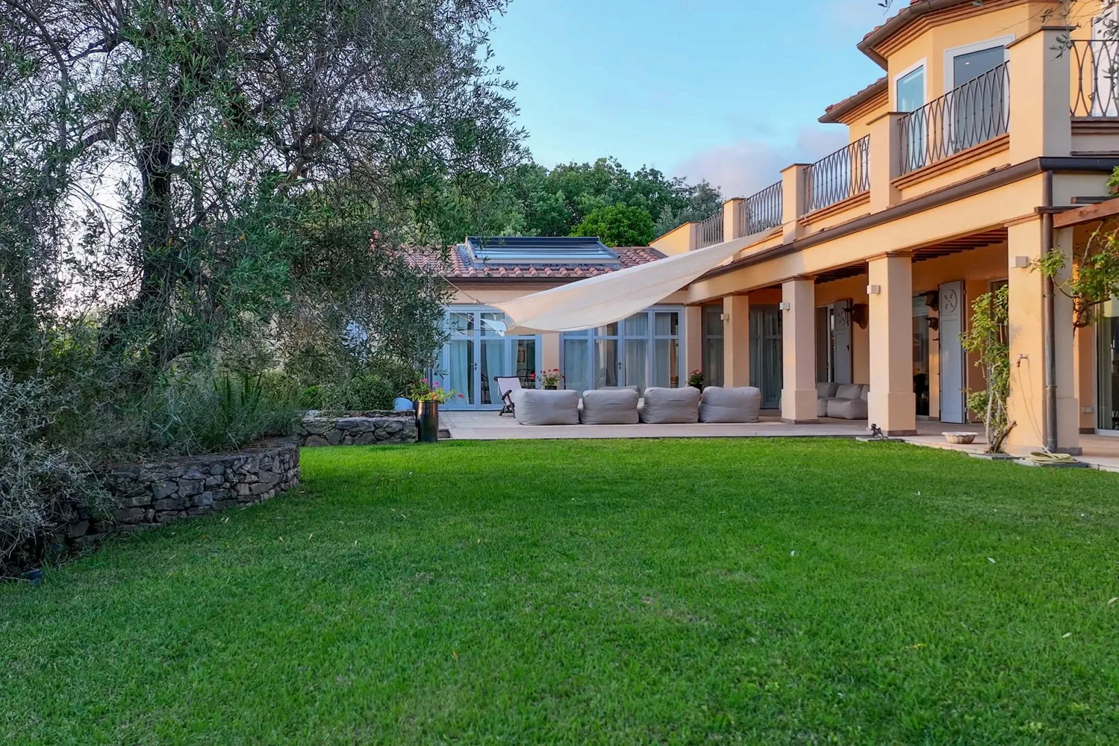 Un césped ajardinado y árboles junto a una casa moderna con patio sombreado.