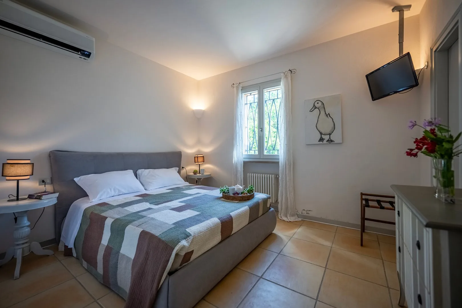 Un dormitorio con una cama tendida, una ventana y mesitas de noche.