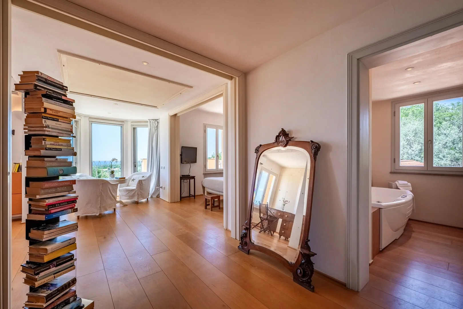 Un dormitorio luminoso con un espejo grande y ventanas hacia habitaciones contiguas.