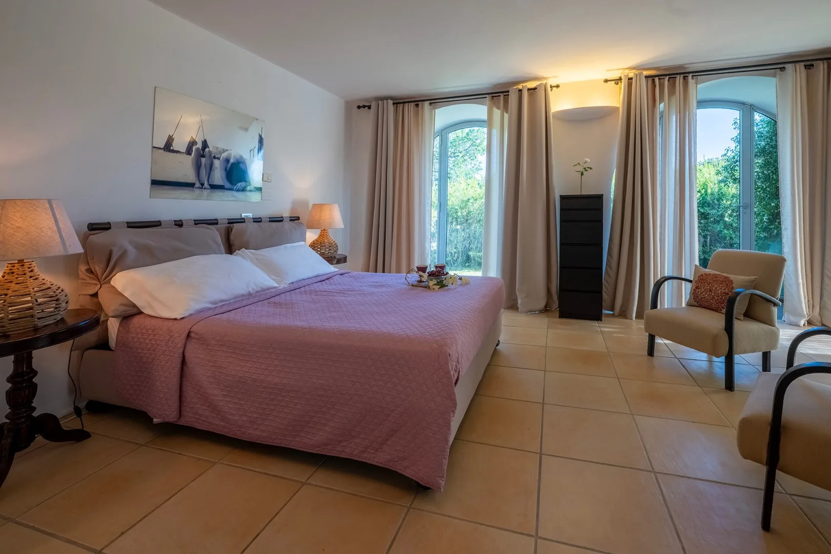 Un dormitorio con una cama grande, dos ventanas altas y una silla.