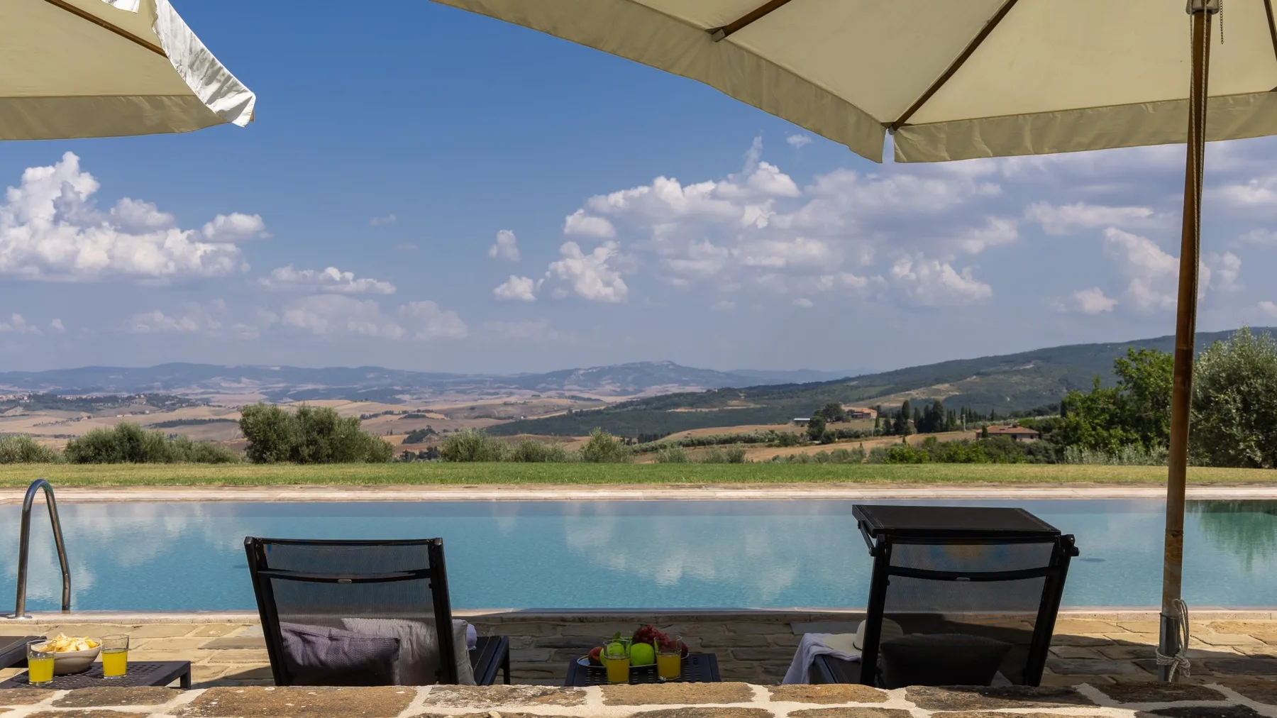 Asientos junto a una piscina exterior contemplan el agua turquesa y las colinas bajo sombrillas.