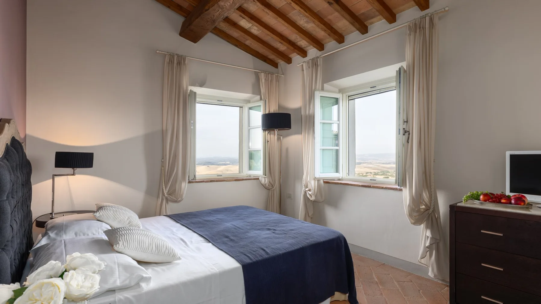 Un dormitorio con una cama, ventanas altas y vigas de madera expuestas en el techo.