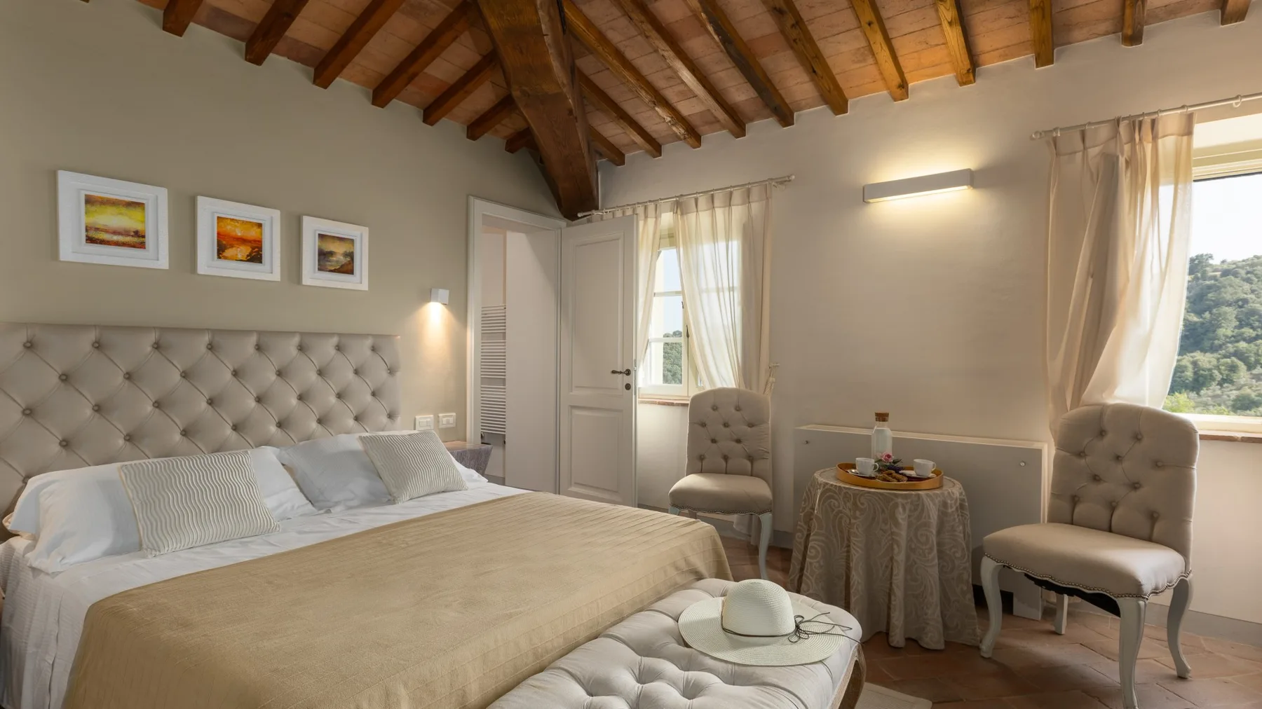 Un dormitorio con una cama, un cabecero acolchado y dos sillones junto a una mesita.