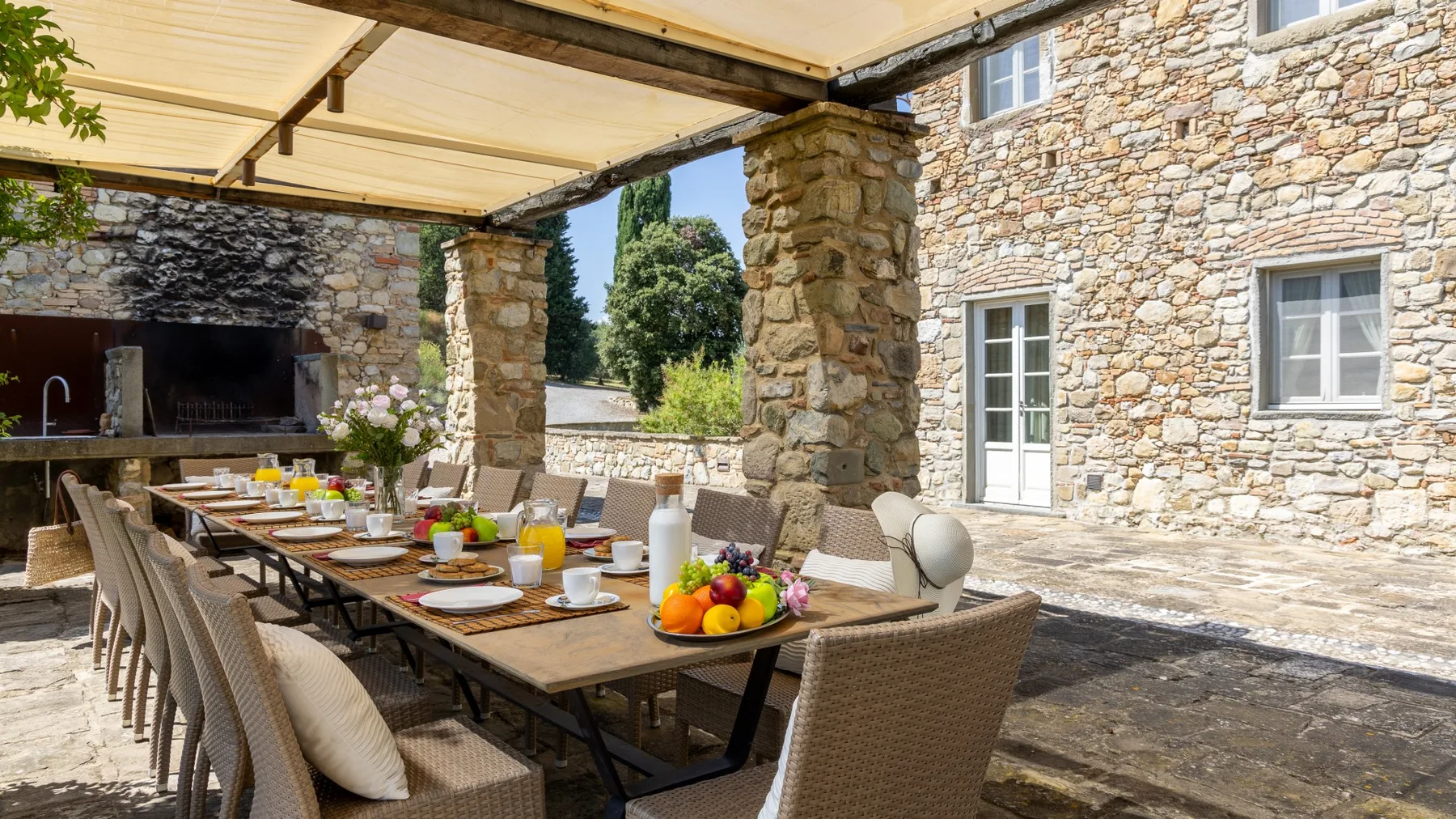 Comedor exterior cubierto con una mesa larga preparada con comida y bebidas.
