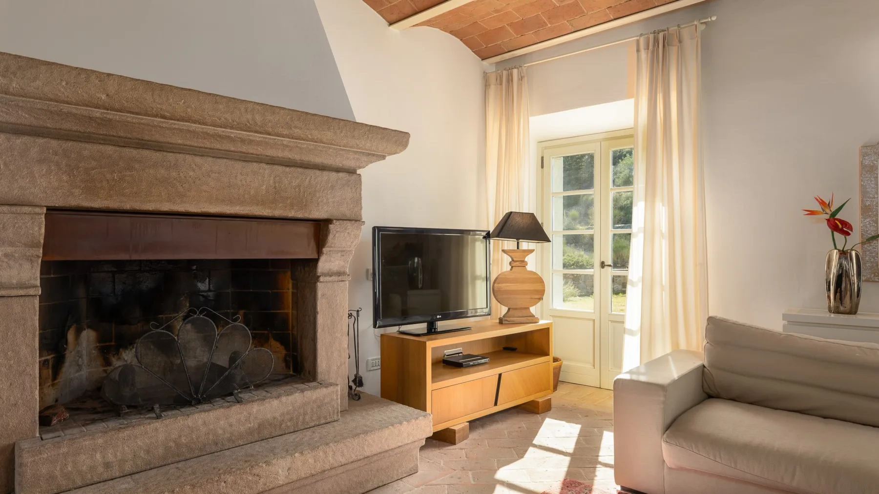 Una sala de estar con chimenea, televisor y asientos junto a una ventana luminosa.