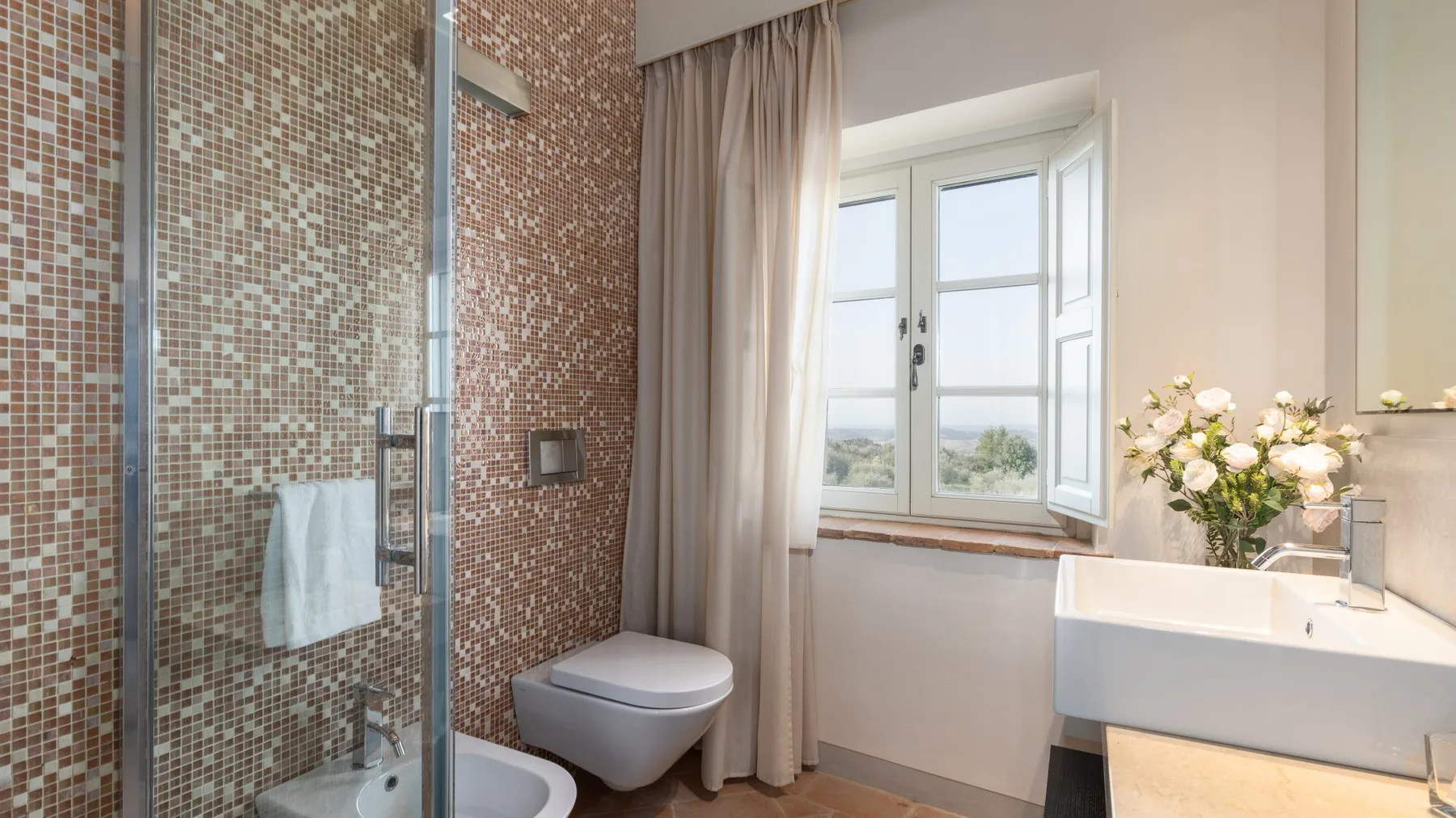 Un baño con ducha alicatada, lavabo y una ventana con cortinas.
