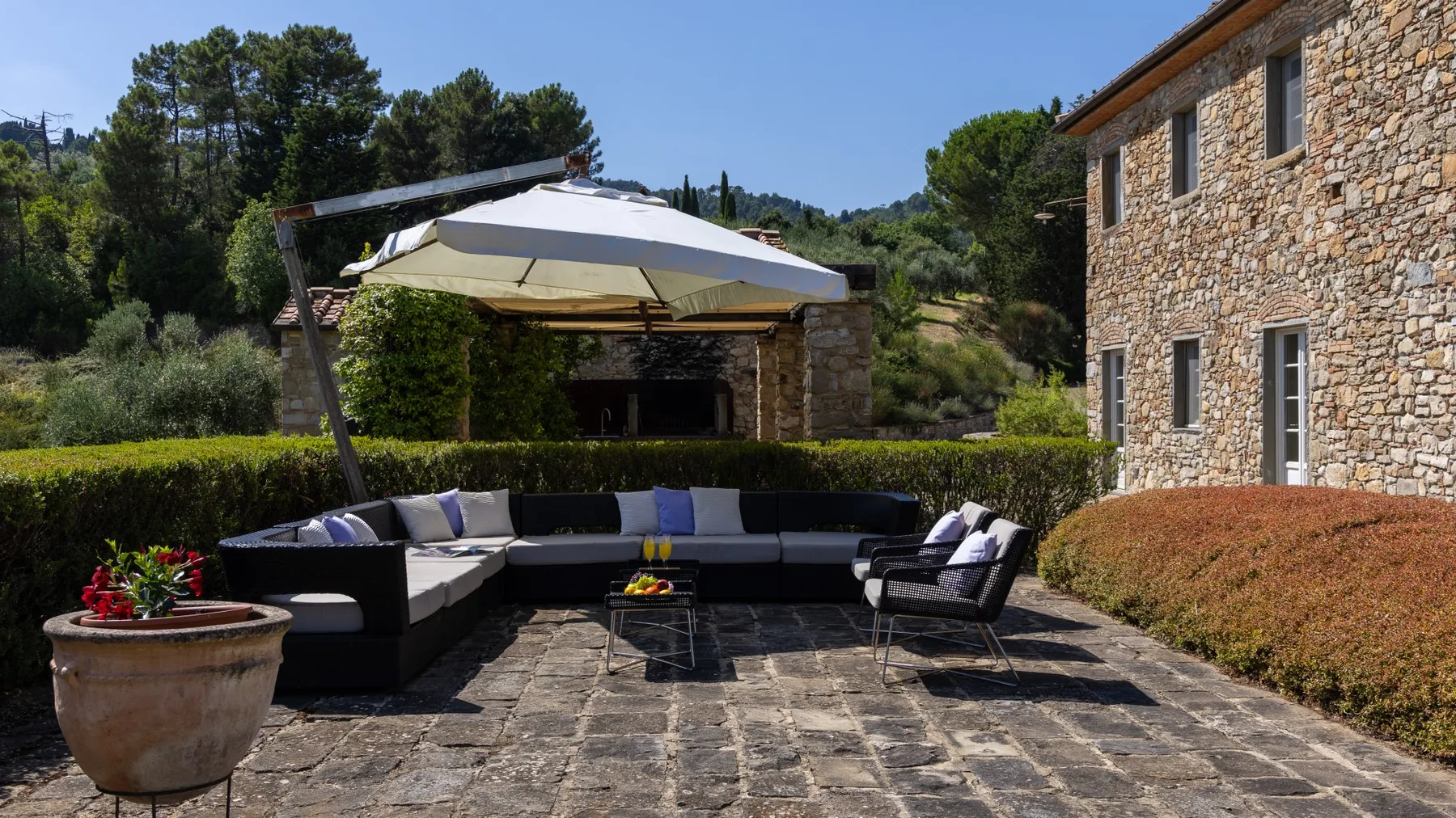 Un patio al aire libre con asientos acolchados bajo una sombrilla grande junto a un edificio de piedra.