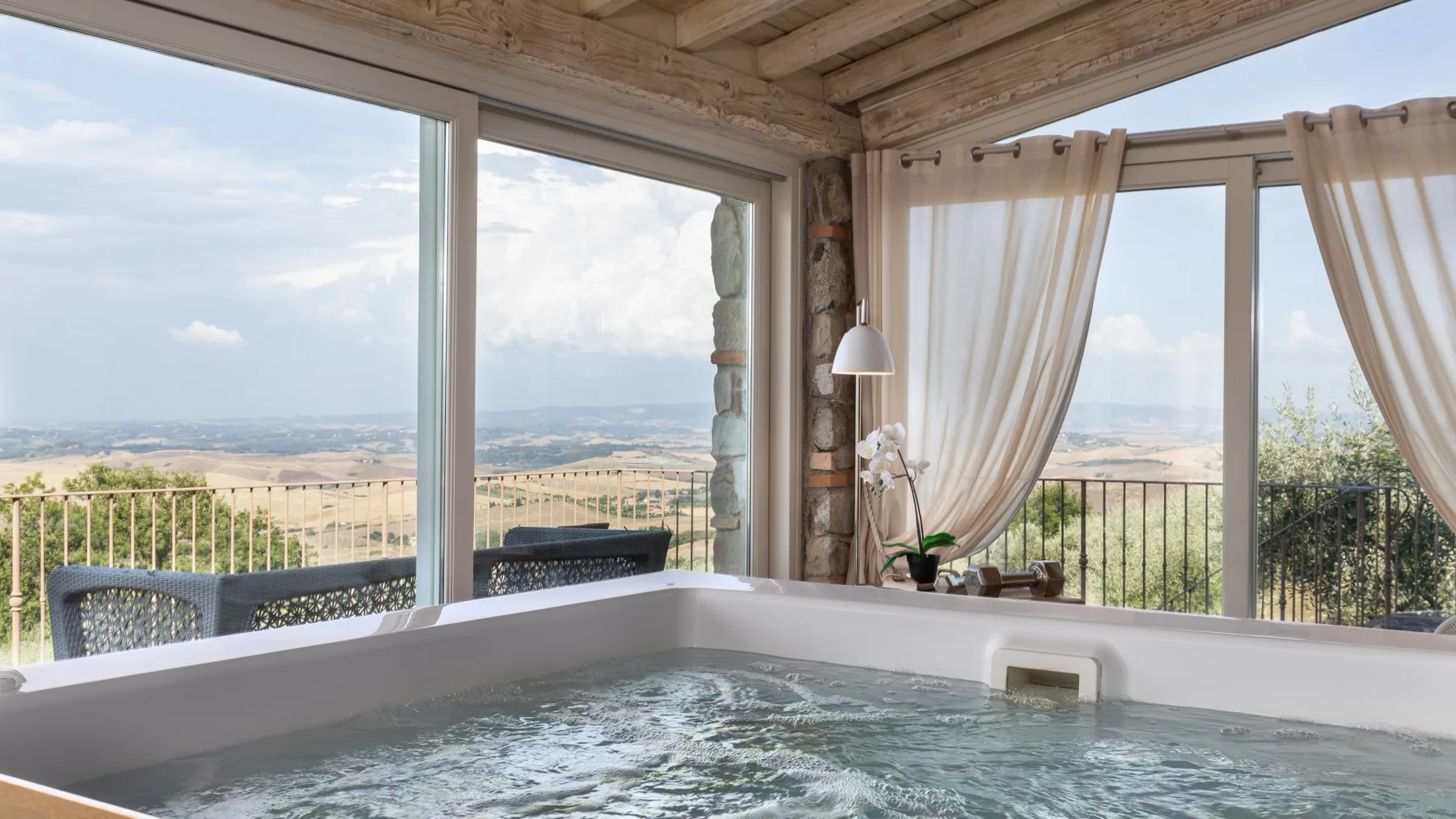 Una bañera de hidromasaje está junto a grandes ventanas con vistas a un paisaje rural.