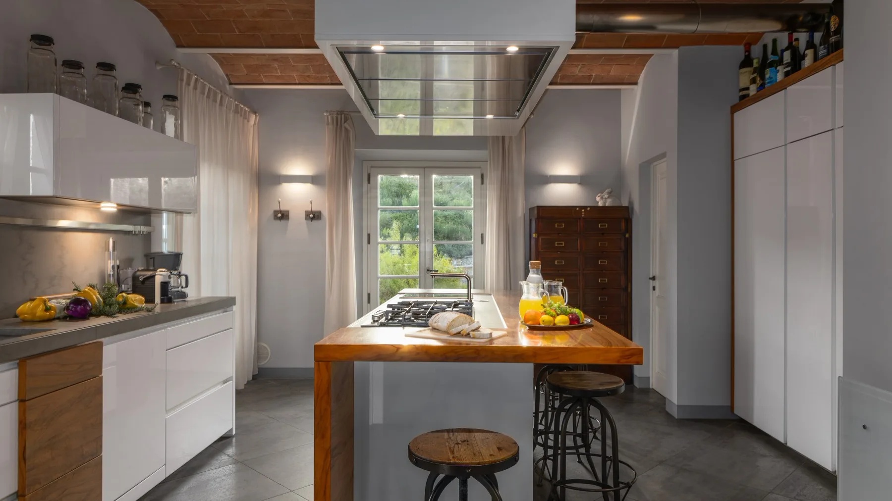 Una cocina con una isla central, taburetes y una ventana con vistas a zonas verdes.