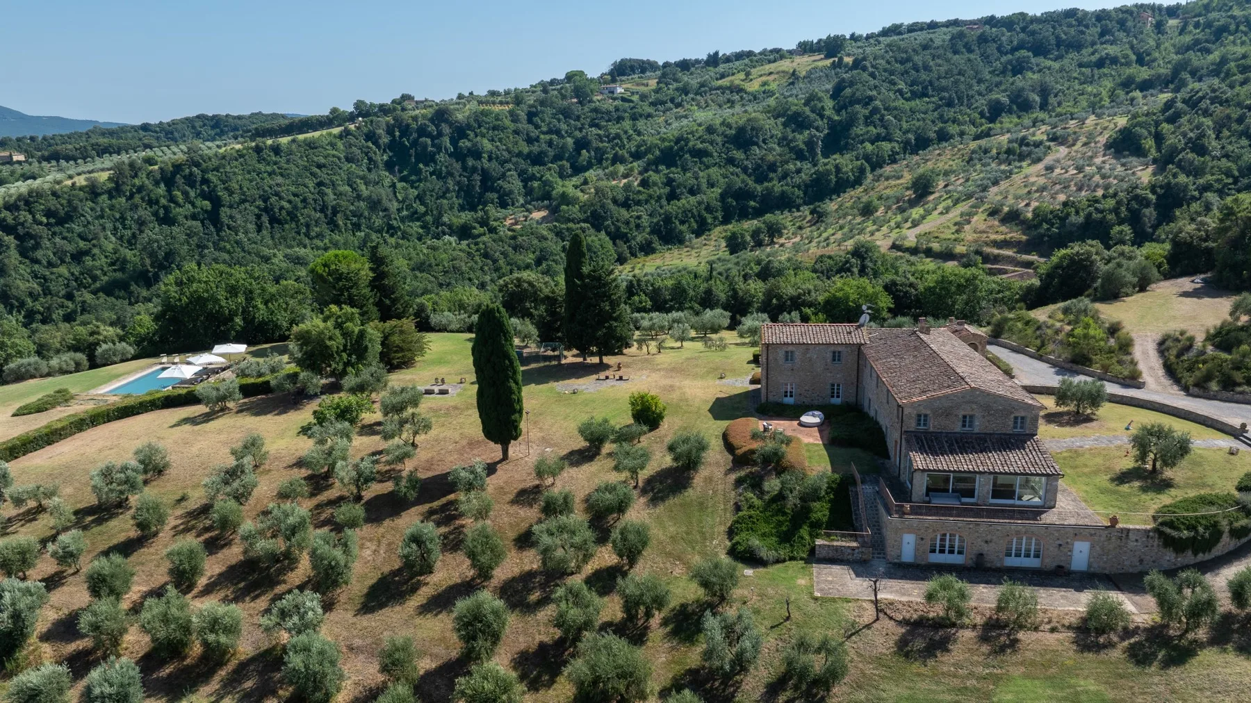 Una casa rural está entre olivos, con colinas boscosas al fondo.