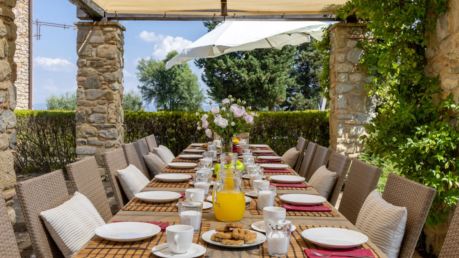 Una mesa al aire libre está puesta con platos y bebidas bajo un toldo.