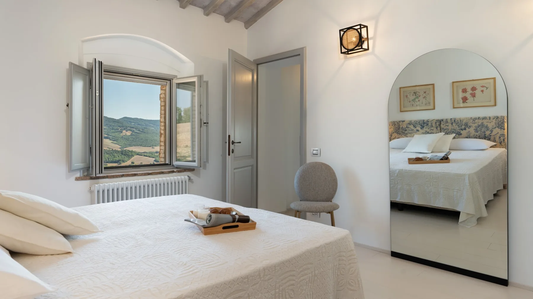 A bedroom with a bed, an open window, and a mirror reflecting another bed.