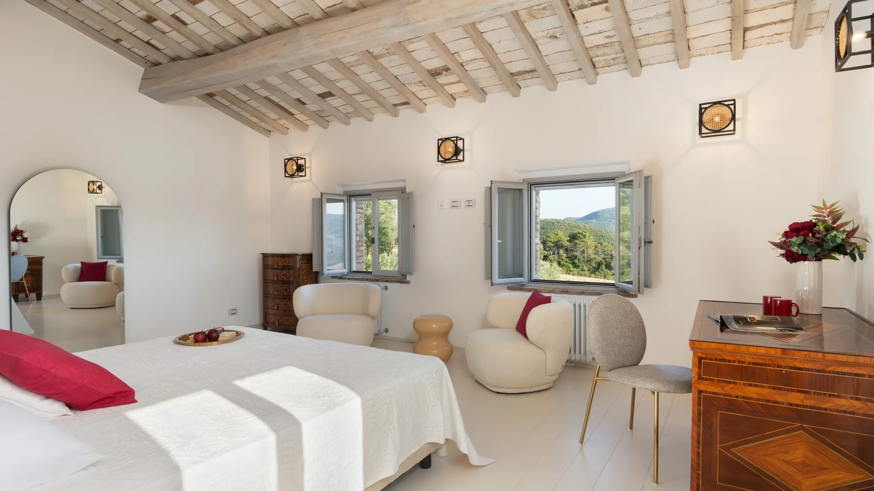 A bright bedroom with a white bed, rounded seating, and open windows.