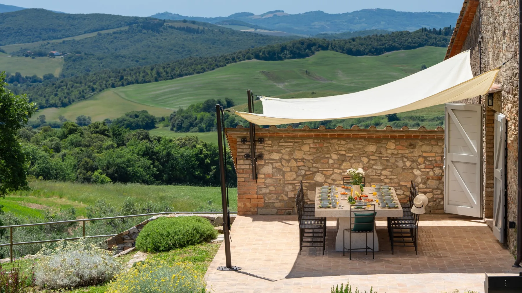 A stone patio with an outdoor dining table overlooks rolling green hills.