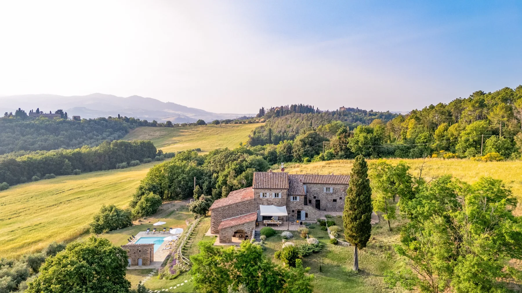 A rural stone house sits amid rolling green hills and fields.